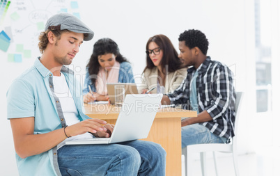 Casual man using laptop with colleagues behind in office