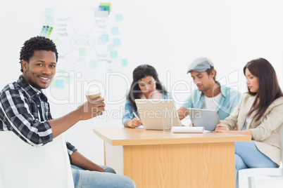 Man holding take away coffee cup with colleagues behind
