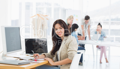 Casual woman at desk with colleagues behind in office