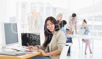 Casual woman at desk with colleagues behind in office