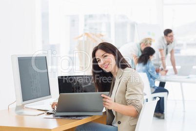 Casual woman working at desk with colleagues behind in office