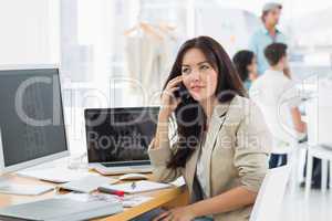 Woman on call at desk with colleagues behind in office