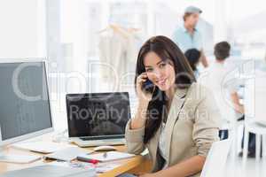 Woman on call at desk with colleagues behind in office