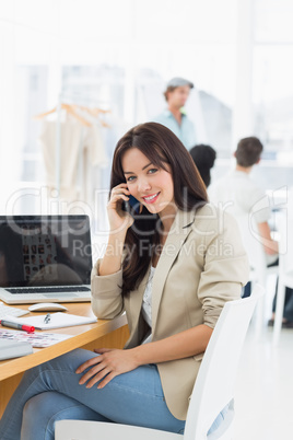 Casual woman on call at desk with colleagues behind in office