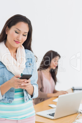 Smiling casual young woman text messaging in office