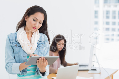 Casual female artist using digital tablet with colleague in back