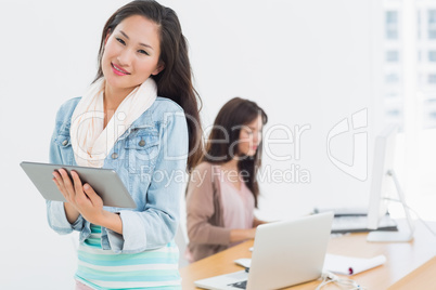 Casual female artist using digital tablet with colleague in back