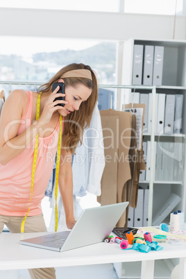 Fashion designer using laptop and cellphone in studio