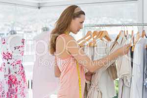 Beautiful fashion designer looking at clothes on rack