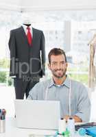 Smiling male fashion designer using laptop in the studio