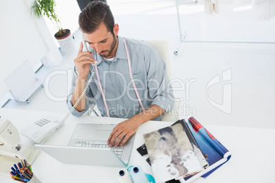 Fashion designer using laptop and phone in studio