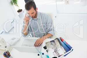 Fashion designer using laptop and phone in studio
