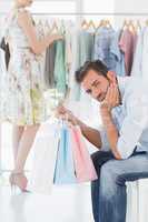 Bored man with shopping bags while woman by clothes rack