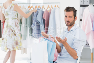 Bored man with shopping bags while woman by clothes rack