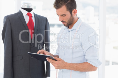 Concentrated fashion designer looking at digital tablet by suit