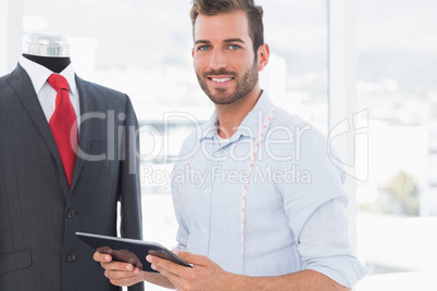 Male fashion designer with digital tablet by suit on dummy