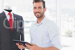 Male fashion designer with digital tablet by suit on dummy