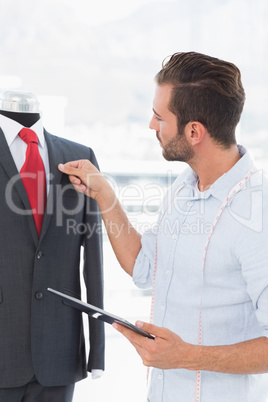 Fashion designer with digital tablet looking at suit on dummy