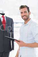 Fashion designer with digital tablet by suit on dummy