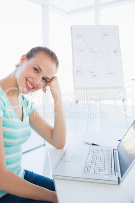 Smiling young casual woman in front of laptop at office