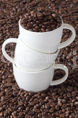 drei kaffeetassen gestaplet stehen zwischen kaffeebohnen