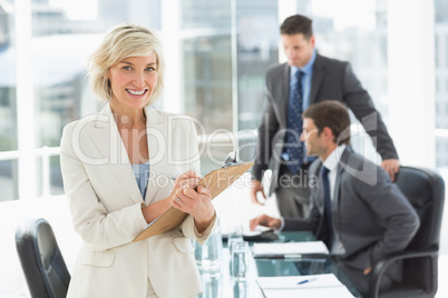 Businesswoman writing on clipboard with colleagues in background