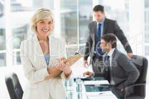 Businesswoman writing on clipboard with colleagues in background