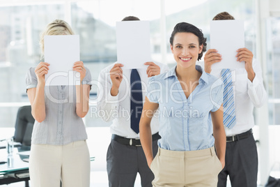 Businesswoman with colleagues holding blank paper in front of fa
