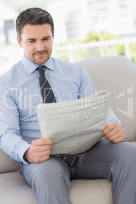 Well dressed young man reading newspaper at home