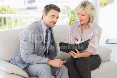 Smart businessman and his secretary  looking at diary on sofa