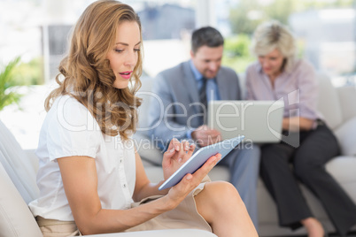 Businesswoman using digital tablet with colleagues using laptop