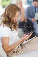 Businesswoman text messaging with colleagues using laptop behind