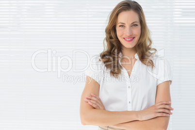 Smiling businesswoman with arms crossed against blinds