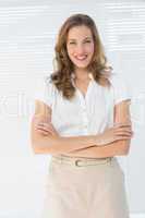 Smiling businesswoman with arms crossed against blinds