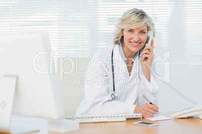 Smiling doctor with computer using phone at medical office
