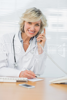 Female doctor using phone while writing notes