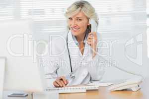 Female doctor with computer using phone at medical office