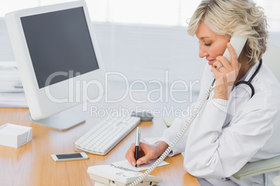 Female doctor using phone while writing notes at office