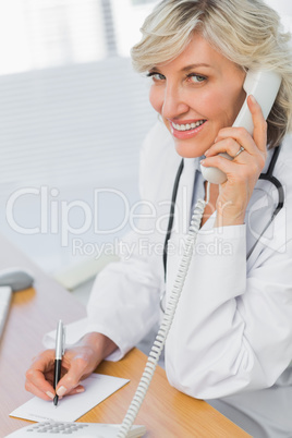 Female doctor using phone while writing notes