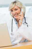 Smiling female doctor using laptop and phone