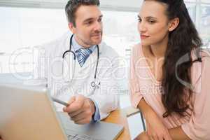 Doctor showing something on laptop to patient in medical office