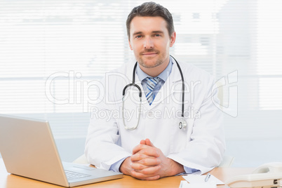 Male doctor with laptop at desk in medical office