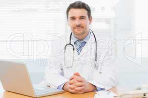 Male doctor with laptop at desk in medical office