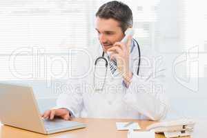 Concentrated doctor using laptop and phone