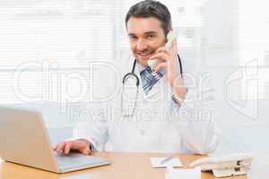 Male doctor using laptop and phone in medical office