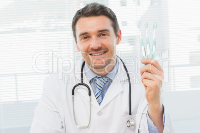 Smiling doctor holding toothbrushes in office