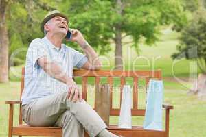 Cheerful relaxed senior man using mobile phone at park
