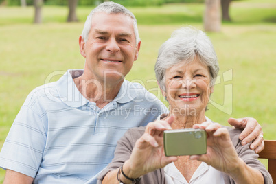 Cheerful senior couple photographing themselves at park