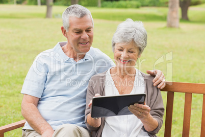 Senior couple using digital tablet on bench at park
