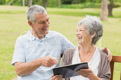 Cheerful senior couple using digital tablet on bench at park